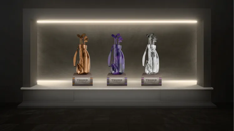 Three illuminated golf bag trophies in bronze, purple, and silver colors on a white pedestal with the name 'TRUMP' engraved on the bases.